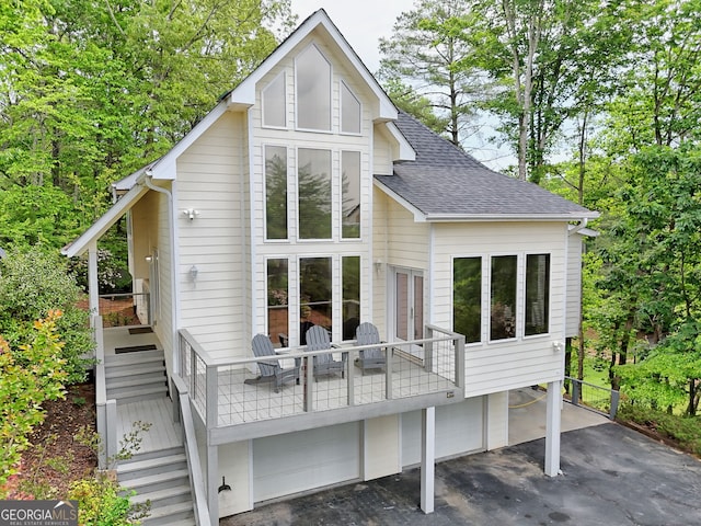 rear view of property featuring a garage, roof with shingles, stairway, and a wooden deck