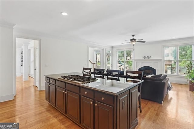 1029 Ector Dr NW, Kennesaw, GA 30152 - kitchen featuring stainless steel gas stovetop, a fireplace, a ceiling fan, light wood-style flooring, and a breakfast bar