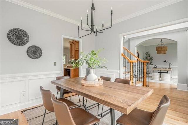 6610 Major Dr, Cumming, GA 30040 - dining space featuring a chandelier, arched walkways, stairway, light wood finished floors, and a wainscoted wall