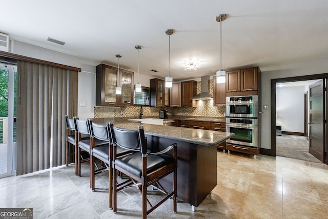 kitchen featuring wall chimney range hood, decorative backsplash, glass insert cabinets, a kitchen bar, and cooktop