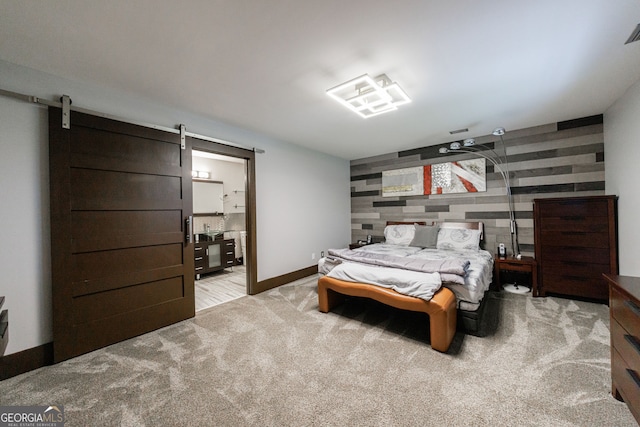 bedroom with an accent wall, a barn door, light carpet, and baseboards