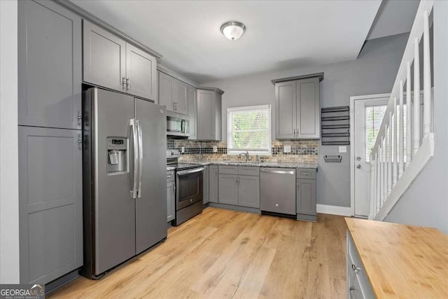 3111 Jones St, East Point, GA 30344 - kitchen featuring stainless steel appliances, gray cabinets, a sink, decorative backsplash, and light wood-style floors