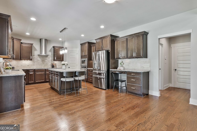 kitchen with stainless steel appliances, wall chimney range hood, dark brown cabinetry, decorative backsplash, and recessed lighting