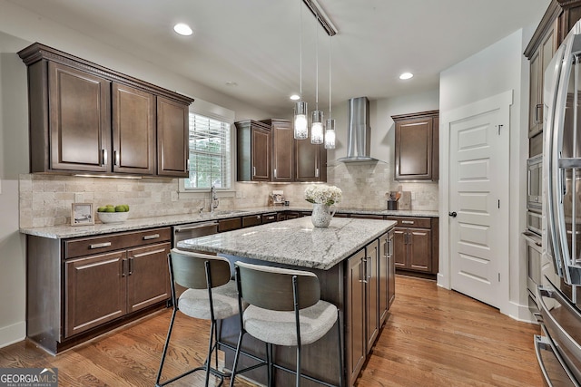 kitchen with wall chimney range hood, a sink, dark brown cabinets, a breakfast bar area, and recessed lighting