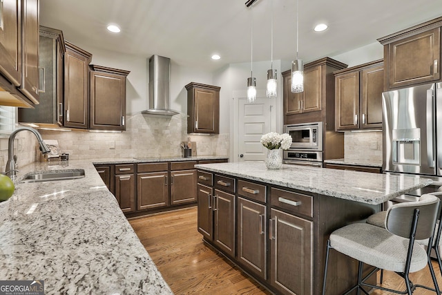 kitchen with wall chimney exhaust hood, appliances with stainless steel finishes, a kitchen bar, a sink, and a center island