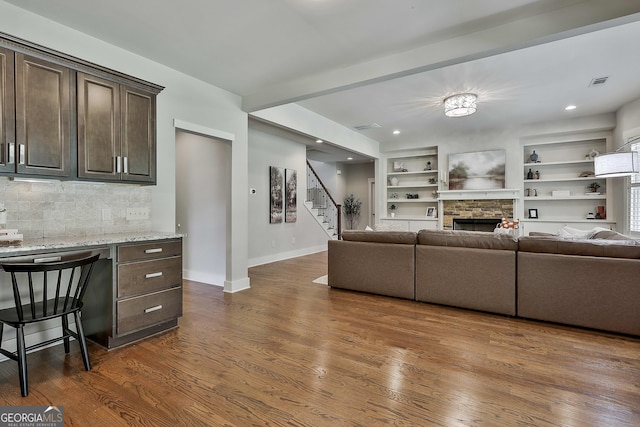 living room with a fireplace, stairs, dark wood-type flooring, baseboards, and built in shelves