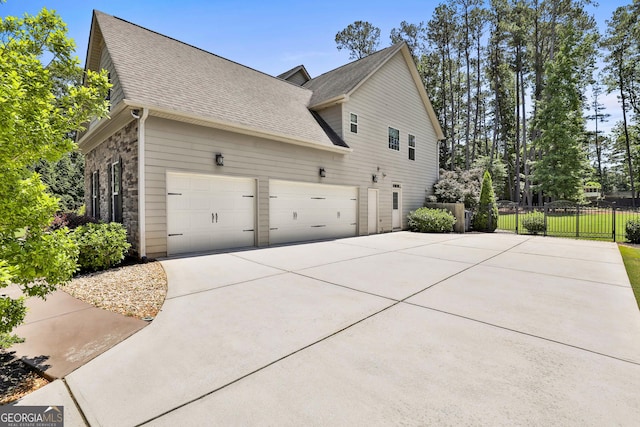 view of property exterior with driveway, a shingled roof, fence, and stone siding