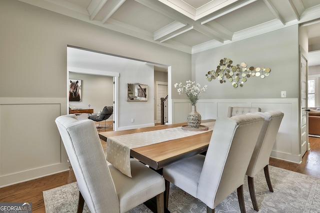dining area featuring coffered ceiling, wood finished floors, beamed ceiling, and a wainscoted wall