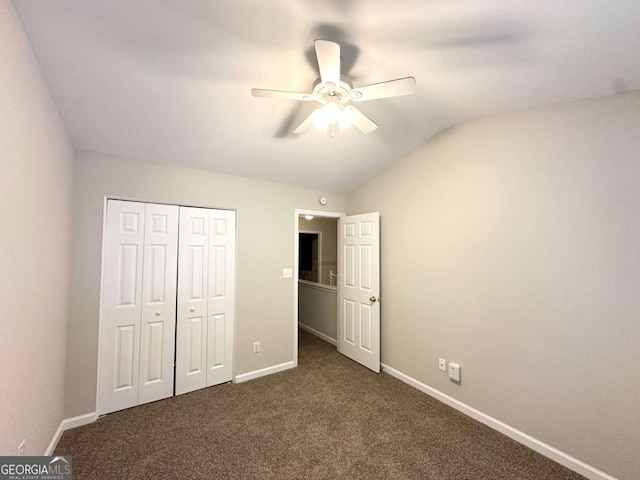 unfurnished bedroom with lofted ceiling, baseboards, dark carpet, a closet, and a ceiling fan