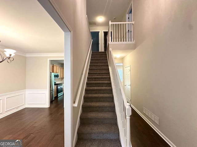 stairway with wood finished floors, a chandelier, a wainscoted wall, and ornamental molding
