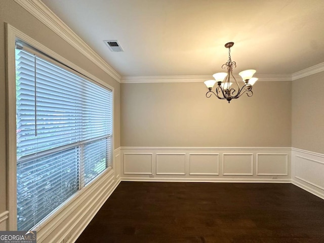 empty room with a chandelier, crown molding, dark wood-type flooring, and wainscoting