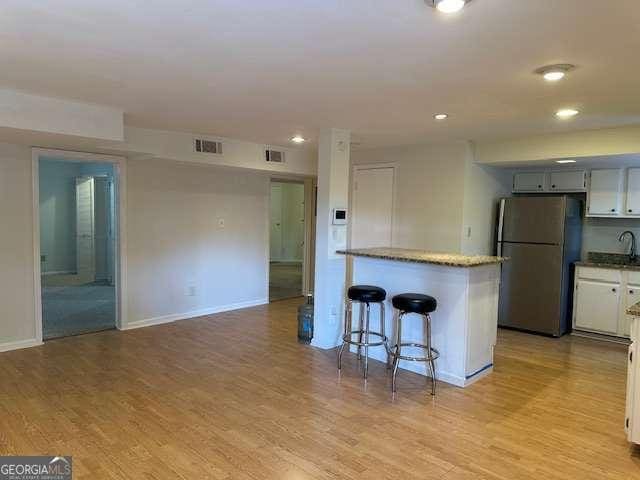 1233 Woodland Ave NE Unit 5, Atlanta, GA 30324 - kitchen featuring freestanding refrigerator, light wood finished floors, white cabinetry, a kitchen bar, and baseboards