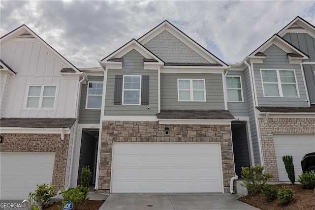 townhome / multi-family property with a garage, stone siding, board and batten siding, and concrete driveway
