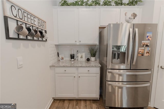 kitchen with stainless steel fridge with ice dispenser, white cabinetry, wood finished floors, backsplash, and light stone counters