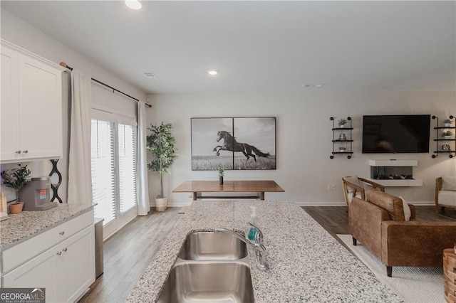 kitchen with recessed lighting, open floor plan, white cabinets, wood finished floors, and a sink