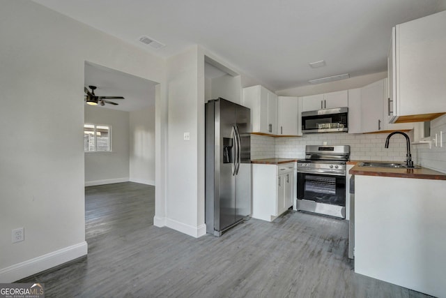 kitchen with appliances with stainless steel finishes, a sink, wooden counters, light wood-style floors, and decorative backsplash