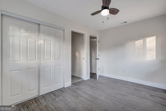 unfurnished bedroom with wood finished floors, baseboards, a closet, and a ceiling fan