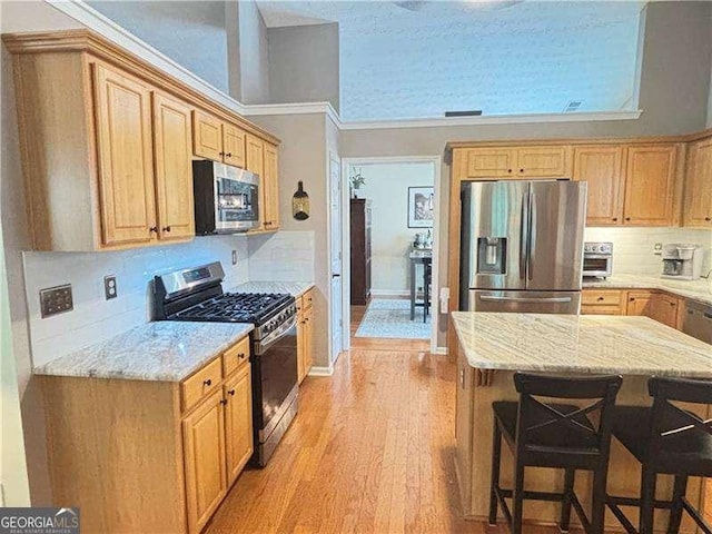 4025 Mcdowell Dr, Acworth, GA 30101 - kitchen with stainless steel appliances, a breakfast bar area, light wood-type flooring, light stone counters, and ornamental molding
