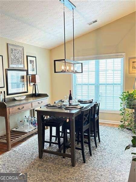 4025 Mcdowell Dr, Acworth, GA 30101 - dining room featuring vaulted ceiling, a textured ceiling, a chandelier, and wood finished floors