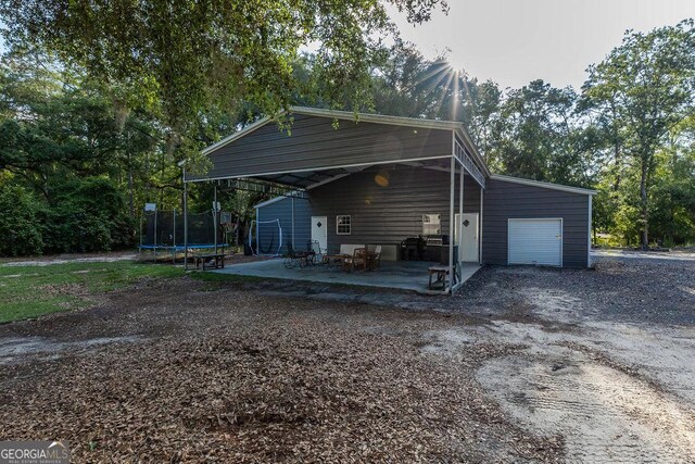 1208 Nease Rd, Guyton, GA 31312 - view of home's exterior featuring a trampoline, a patio, dirt driveway, and a detached garage