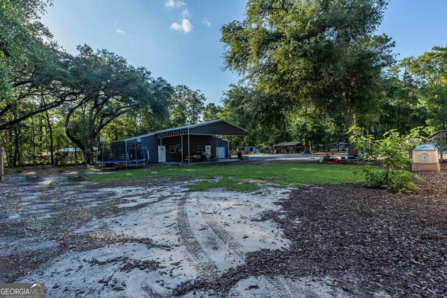 1208 Nease Rd, Guyton, GA 31312 - view of grassy yard with a trampoline, an outbuilding, a carport, and a garage