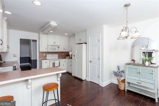 kitchen featuring white appliances, a sink, a peninsula, a chandelier, and dark wood-style flooring