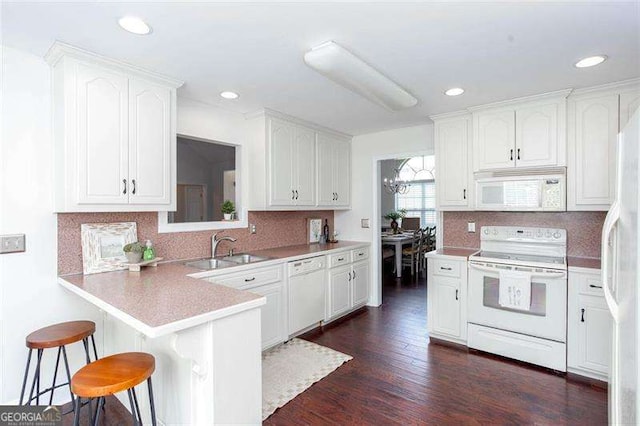 kitchen with white appliances, a sink, a breakfast bar area, white cabinets, and recessed lighting