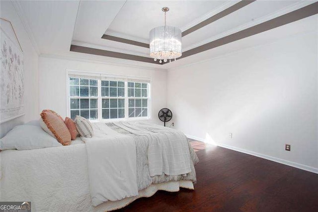 bedroom with a chandelier, wood finished floors, ornamental molding, baseboards, and a raised ceiling