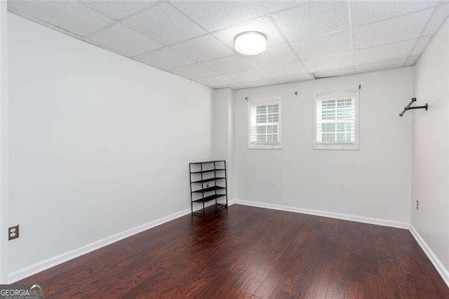empty room featuring wood finished floors, a drop ceiling, and baseboards