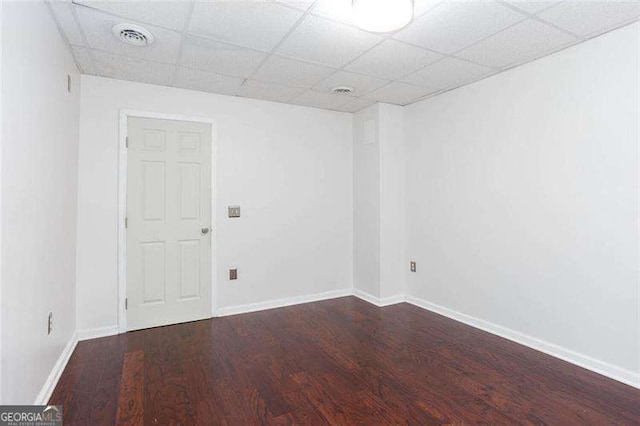 empty room featuring wood finished floors, a drop ceiling, and baseboards