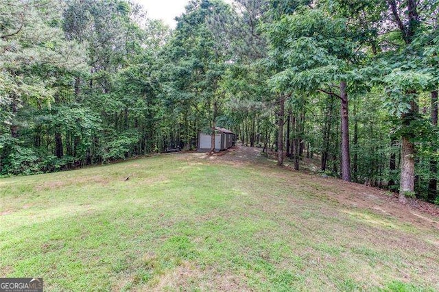 view of grassy yard with a storage unit, an outbuilding, a forest view, and a garage