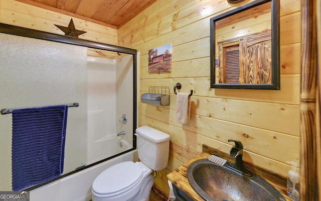 bathroom featuring wood walls, wood ceiling, bath / shower combo with glass door, a sink, and toilet