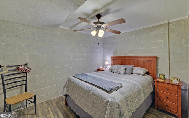 bedroom with dark wood-style floors, concrete block wall, and ceiling fan