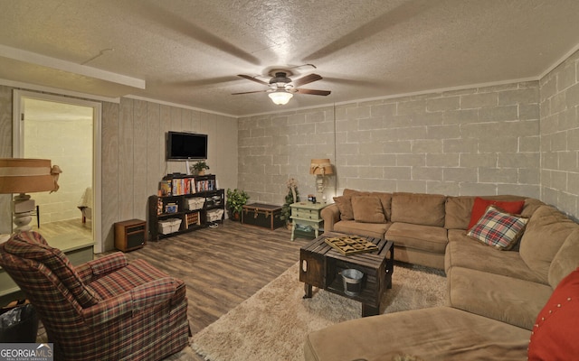 living area featuring wood finished floors, concrete block wall, ceiling fan, a textured ceiling, and ornamental molding