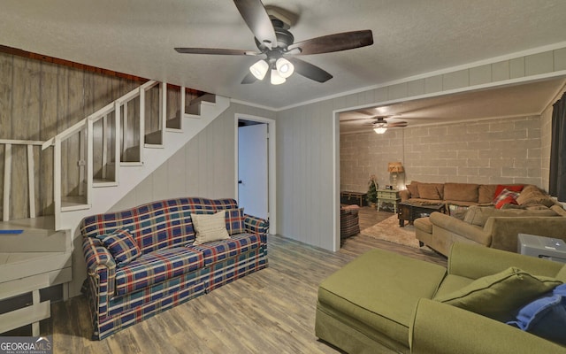 living room featuring ceiling fan, wood finished floors, a textured ceiling, and stairs