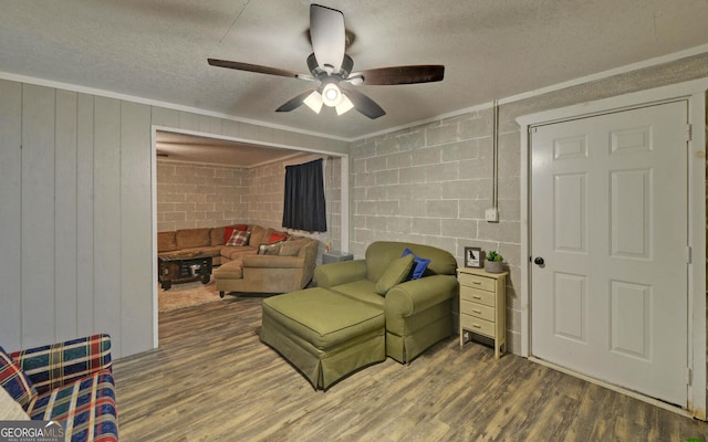 living room featuring a textured ceiling, ceiling fan, concrete block wall, and wood finished floors