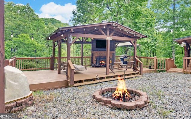 wooden deck with a warm lit fireplace, a gazebo, a fire pit, and grilling area