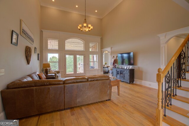 living area with a towering ceiling, stairs, light wood-style flooring, a chandelier, and baseboards