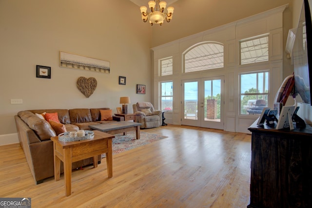 living room with a chandelier, a towering ceiling, light wood finished floors, healthy amount of natural light, and french doors