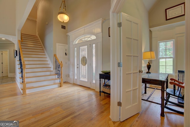 entrance foyer with high vaulted ceiling, light wood-type flooring, stairway, and arched walkways