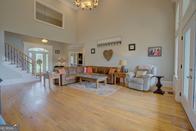 living area featuring a high ceiling, stairs, light wood-style flooring, a chandelier, and baseboards