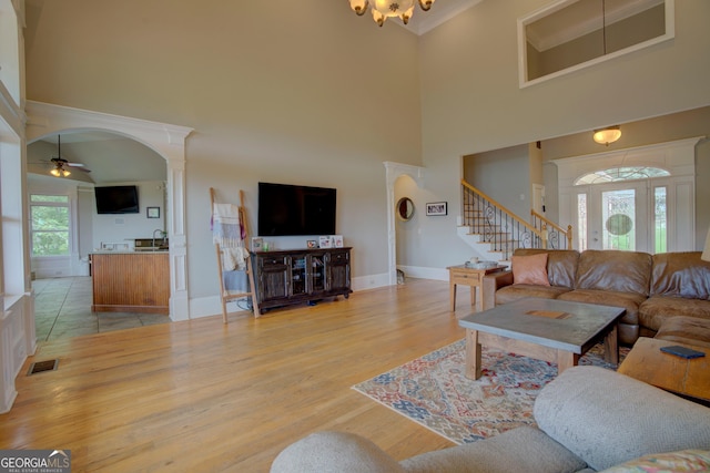 living room with a towering ceiling, stairway, light wood finished floors, baseboards, and a ceiling fan
