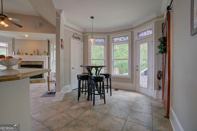 dining area featuring ceiling fan, baseboards, crown molding, a tiled fireplace, and a barn door