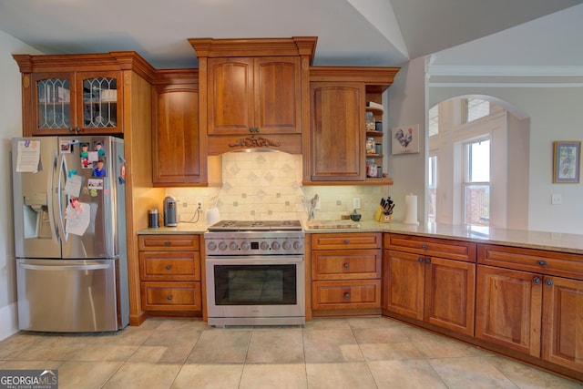 kitchen featuring appliances with stainless steel finishes, arched walkways, decorative backsplash, brown cabinets, and ornamental molding