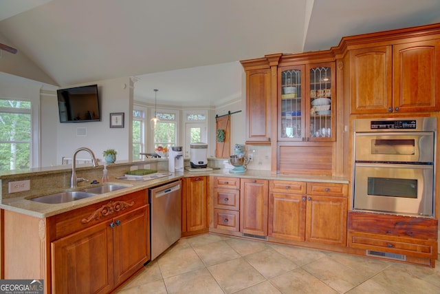 kitchen featuring a sink, stainless steel appliances, a peninsula, light stone countertops, and plenty of natural light