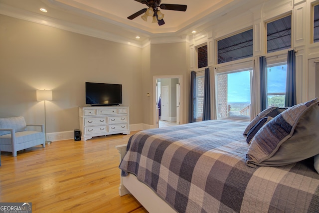 bedroom featuring a high ceiling, crown molding, baseboards, light wood-type flooring, and a tray ceiling
