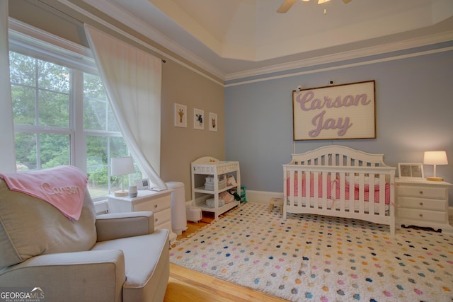 bedroom with a nursery area, crown molding, wood finished floors, a raised ceiling, and baseboards