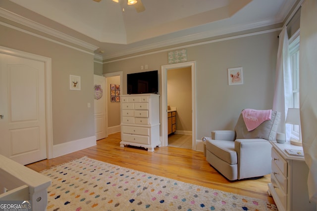 living area featuring light wood-style flooring, a raised ceiling, a ceiling fan, ornamental molding, and baseboards