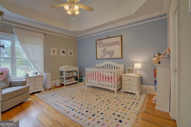 bedroom with a raised ceiling, wood finished floors, a nursery area, ornamental molding, and baseboards