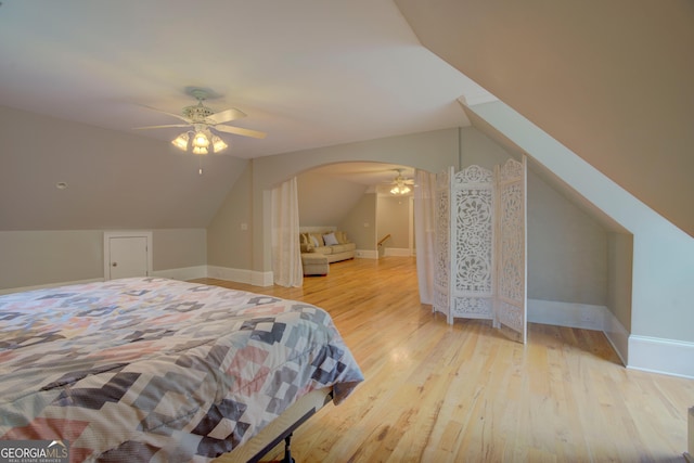 bedroom featuring wood finished floors, vaulted ceiling, arched walkways, ceiling fan, and baseboards